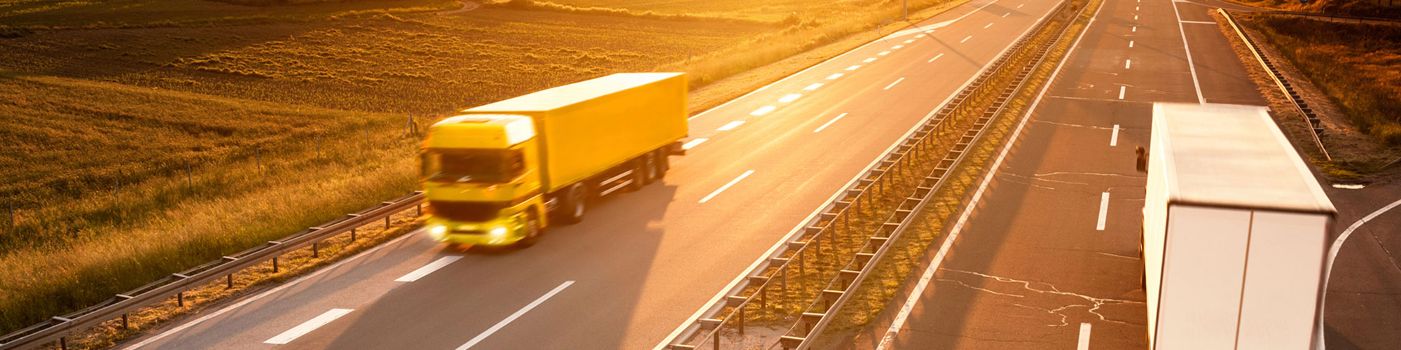 Gul lastbil som kör på motorväg i morgonljus