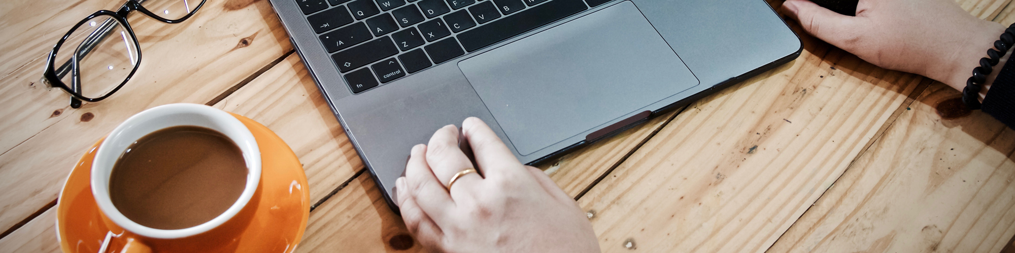 Hand som skriver på en laptop med en kopp kaffe och ett par glasögon vid sidan av