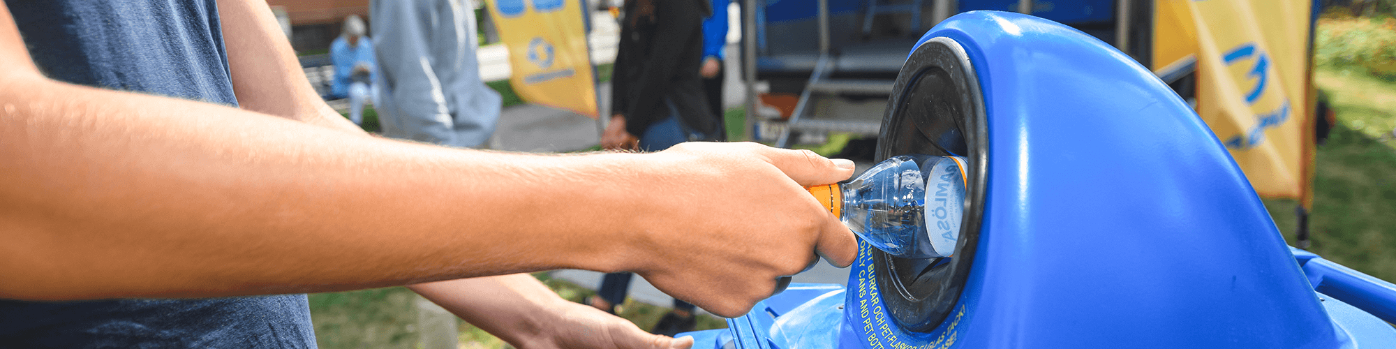 Hand som lämnar en flaska i ett pantkärl i stadsmiljö