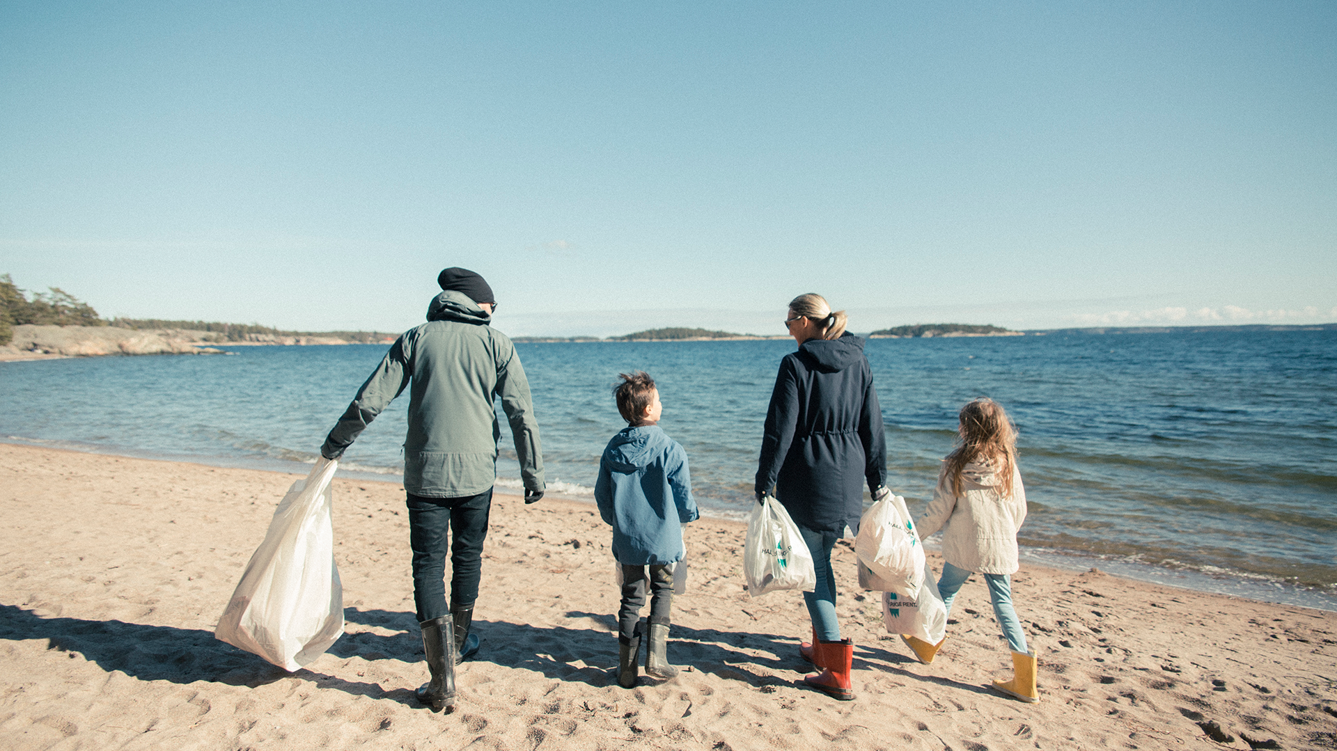 Mamma, pappa och två barn samlar skräp på en strand